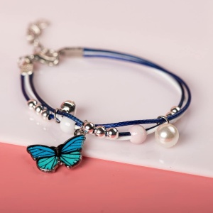 Armband met blauwe vlinderhanger met witte parels op een witte en roze achtergrond