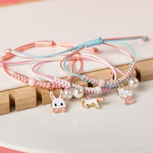 Gevlochten armband met parelhanger en roze en blauw diertje op een witte en houten achtergrond