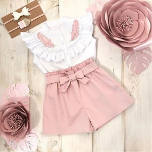 Effen gekleurde shorts met een roze en wit meisjesshirt met roze planten op de zijkant en een houten achtergrond