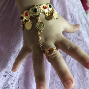 Armband en ring verbonden door een ketting voor een klein meisje aan een kinderhand met een witte rok