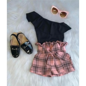 Roze geruite korte broek met zwart shirt, roze zonnebril en glimmende zwarte schoenen op een wit tapijt