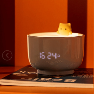 Nachtlampje in de vorm van een theekopje met wekker met een kat op een tijdschrift en een oranje achtergrond