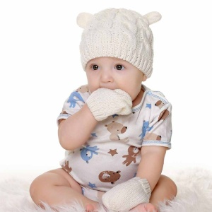 Witte baby winter muts en wanten set met baby met zijn hand in zijn mond en witte gedessineerde kleding