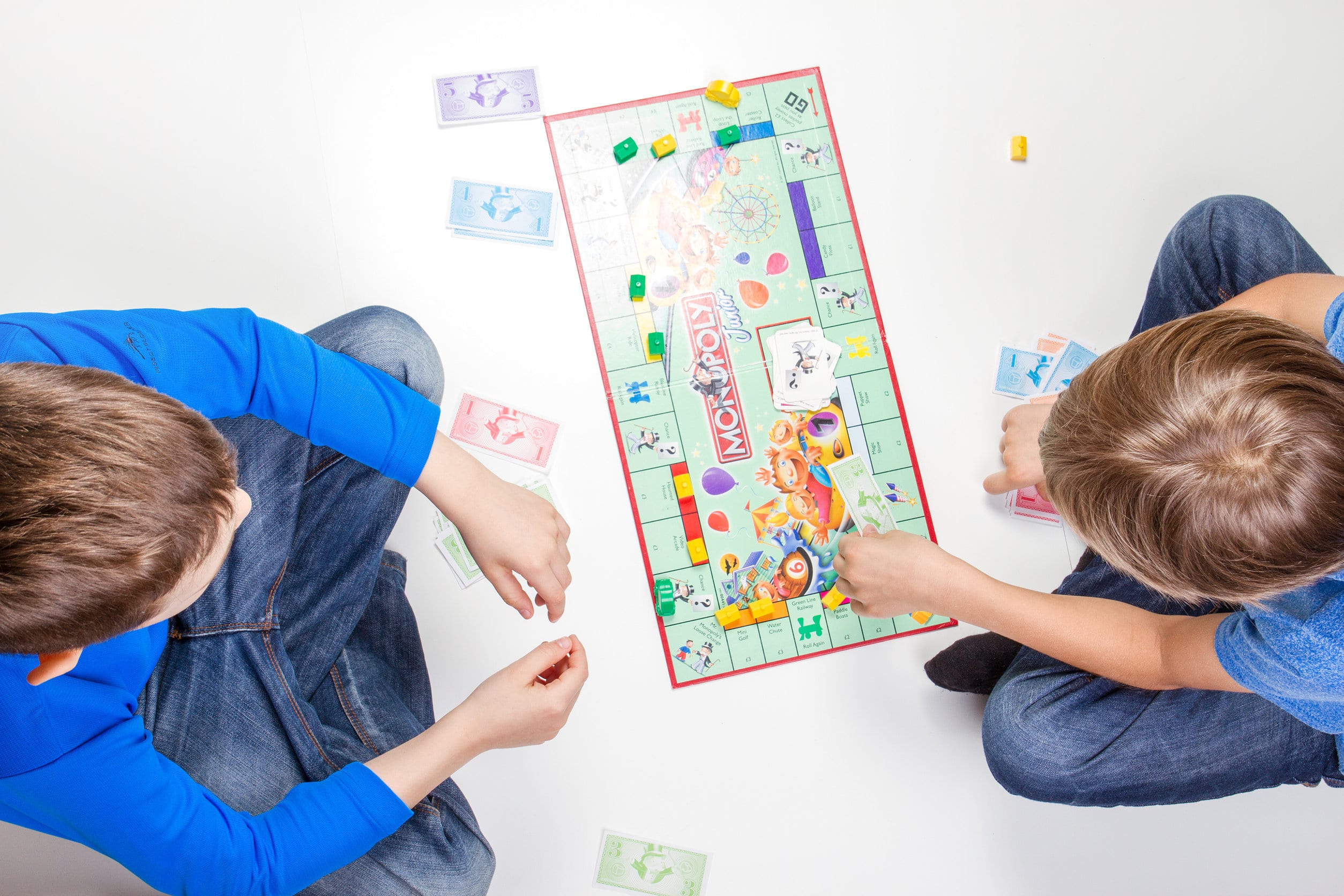 Twee jonge kinderen spelen monopoly, de ene in een blauwe trui, de andere in een blauw T-shirt