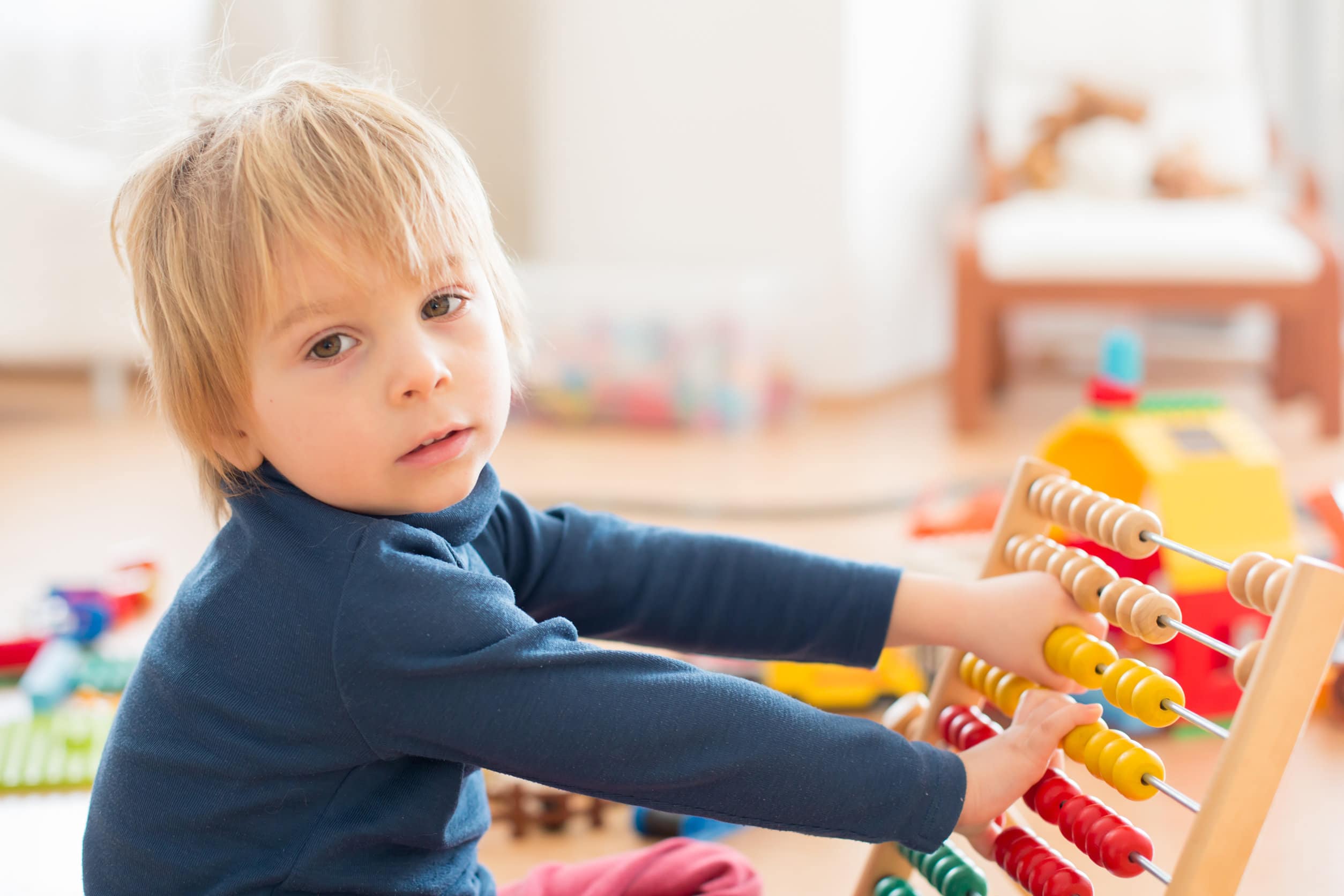 Een jongetje met halflang blond haar en een blauwe trui speelt met een gekleurd telraam om te leren tellen