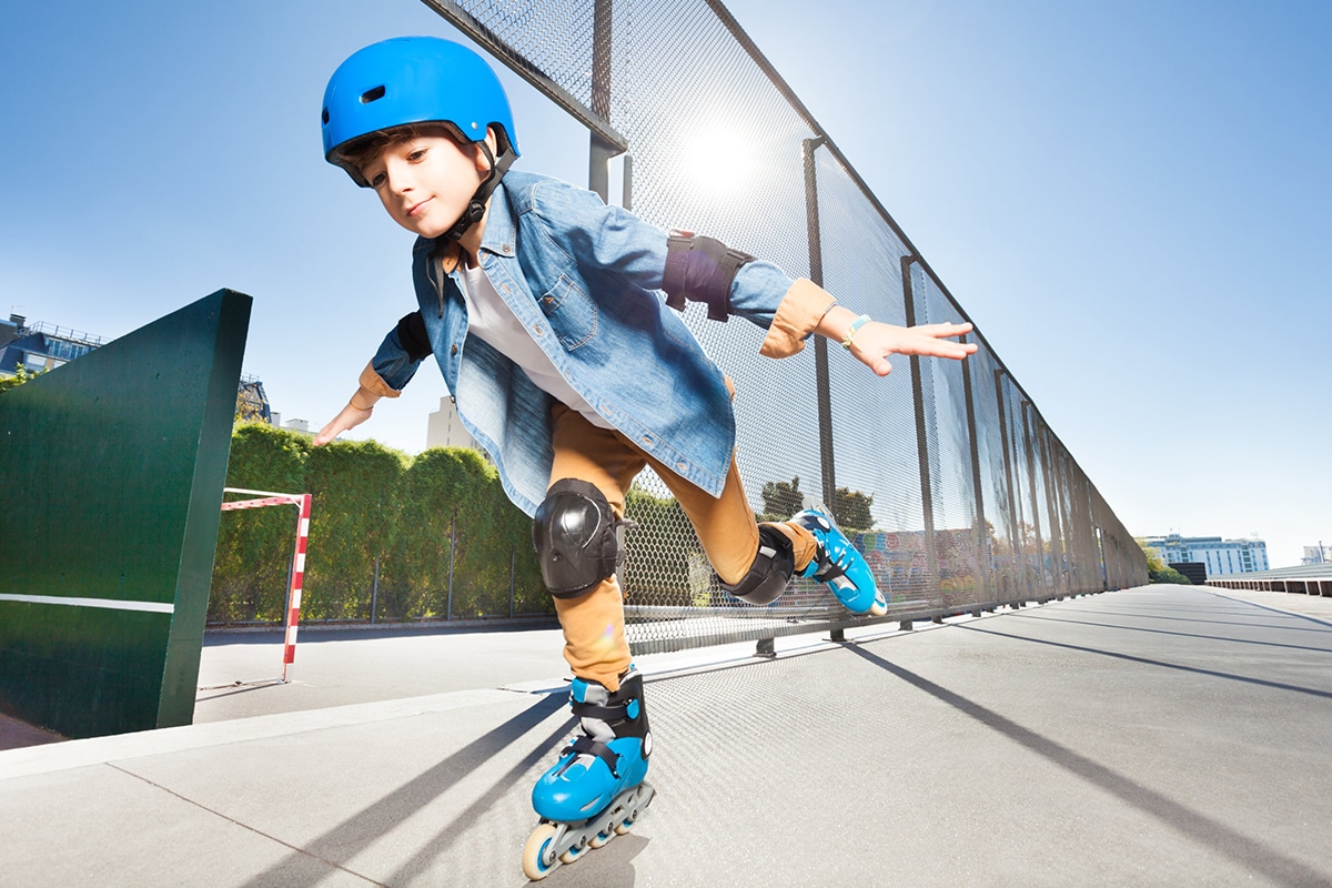 Een jonge jongen zwerft door de straten. Hij draagt een paar blauwe rolschaatsen, zwarte knie- en elleboogbeschermers en een blauwe helm.