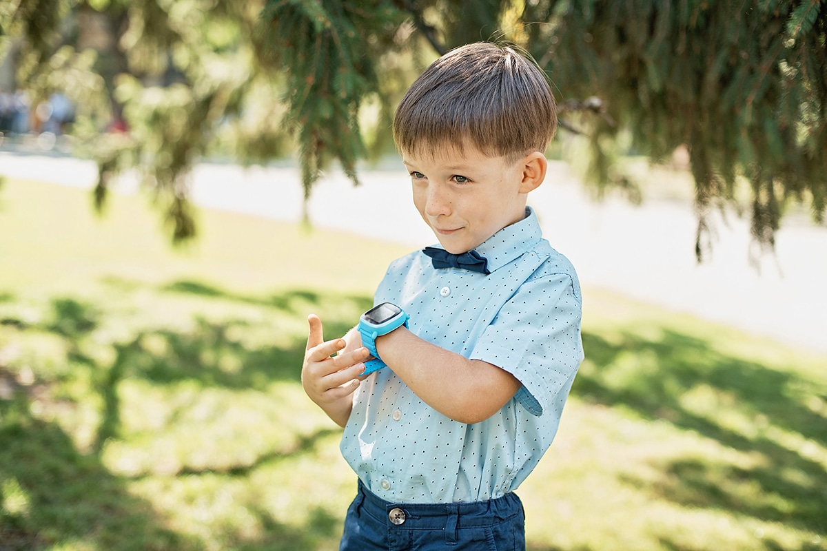 Een jonge jongen oefent op de klok. Hij draagt een blauw horloge, een blauw shirt en hij is buiten in de zon. Zij zijn op het winkelcentrum