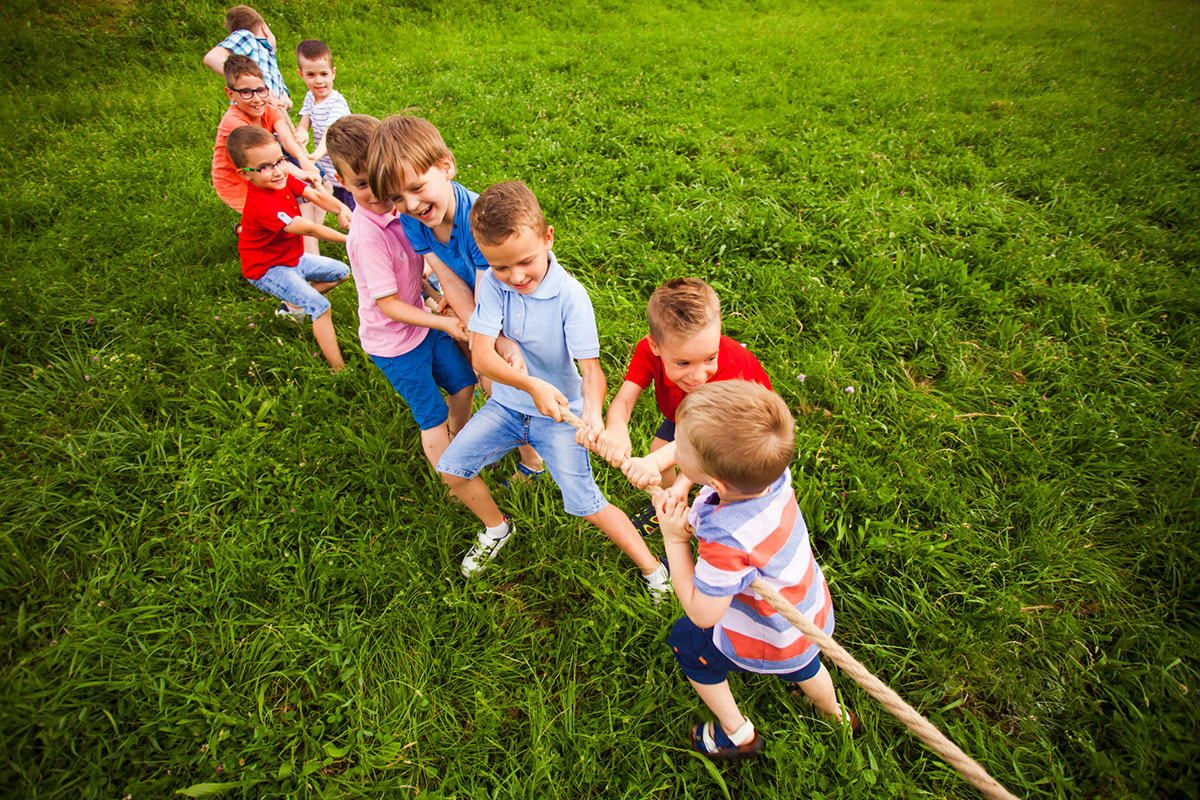Een groep van 9 jonge jongens speelt een spelletje touwtrekken op een stuk groen gras