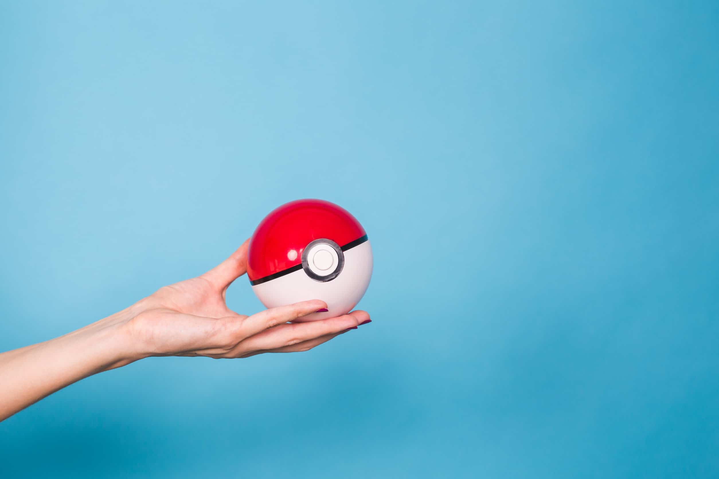 Een hand die een rode en witte pokémon pokeball op een blauwe achtergrond houdt