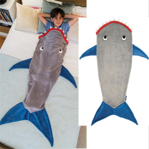 De foto bestaat uit twee delen, het eerste deel toont een kind dat in bed ligt, ingestopt in een grijze haaivormige slaapzak met blauwe vinnen en een rode bek. Het tweede deel van de afbeelding toont deze slaapzak op een witte achtergrond.