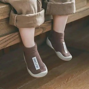 we zien de benen van een zittend kind met bruine sokken met een wit label