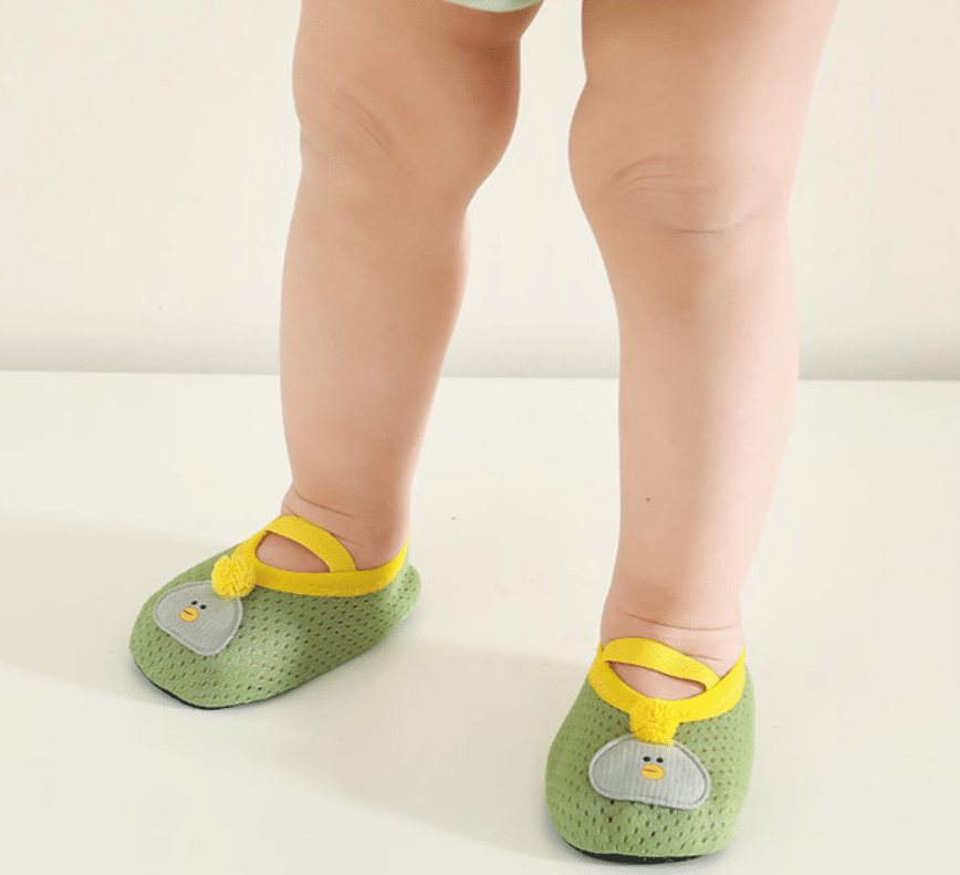 een baby staat met alleen zijn benen zichtbaar en draagt kleine, zachte, ademende groene slofjes