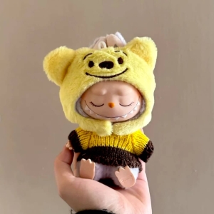 Knuffeloutfit met gele capuchon met lachende oren en geel-bruin gestreepte trui, gedragen door een slapende Labubu-pop.