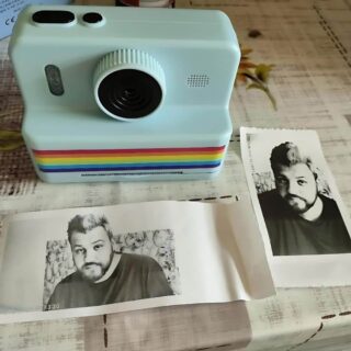 Appareil photo design rétro avec imprimante intégrée, dans sa version bleue, posé sur une table avec des photos imprimées en noir et blanc devant.