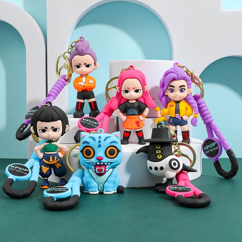 Lot de 6 porte-clés K-pop Demon Hunters représentant les personnages du film, la pie et le tigre bleu. Posés sur des supports blancs. Le sol et le fond sont verts.